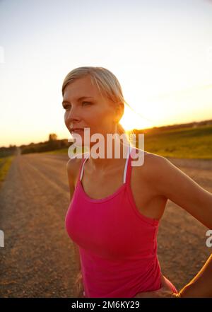 Felicemente raggiungere i suoi obiettivi di fitness. Un bellissimo sportivo in piedi con le mani sui fianchi mentre il sole tramonta sullo sfondo. Foto Stock