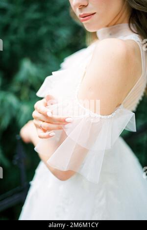 Sposa in un abito bianco tocca il pizzo sulla spalla con le dita. Primo piano Foto Stock