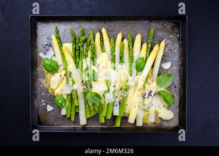 Tradizionale asparagi bianchi e verdi al forno con formaggio e salsa hollandaise servito come vista dall'alto su un vassoio rustico Foto Stock