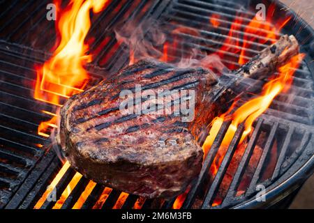 Barbecue wagyu tomahawk bistecca invecchiata a secco offerto come primo piano su una griglia a carbone con fuoco e fumo Foto Stock