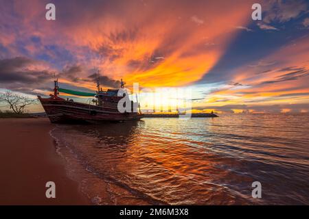 Splendido tramonto sulla riva del mare con una barca da pesca e ondate d'acqua dorate riflesse dal cielo. Foto Stock