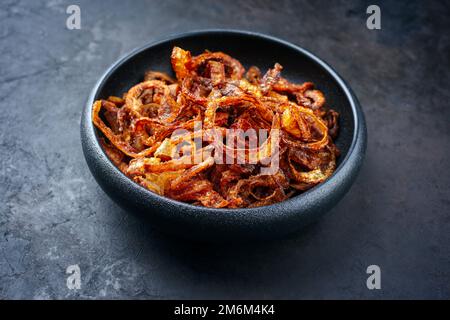 Tradizionali anelli di cipolle croccanti fritti con farina e peperoncino servito come primo piano in un recipiente dal design rustico con spazio per le copie Foto Stock