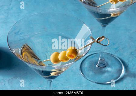 Martini, due bicchieri con olive speziate, su sfondo blu Foto Stock