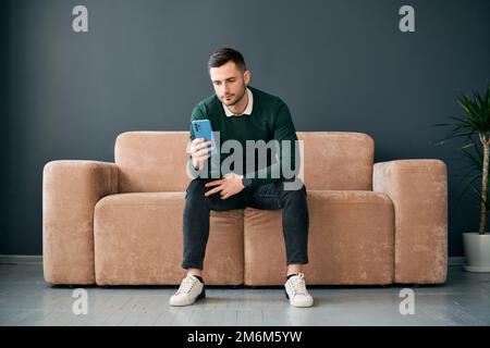 Uomo rilassato seduto sul divano con il telefono cellulare hsi Foto Stock