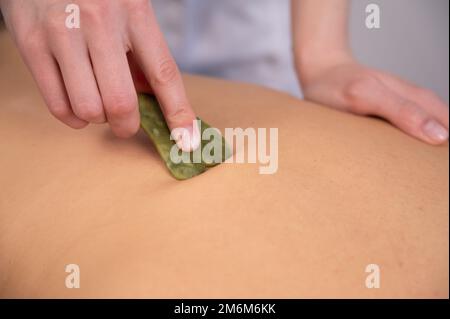 Il massaggiatore fa un massaggio alla schiena con un raschietto per gouache a una cliente femminile. Foto Stock