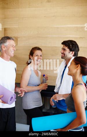 Chiacchierare in palestra. Giovane coppia e coppia matura in abbigliamento sportivo che parlano tra loro. Foto Stock