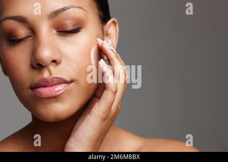 Le più eque di tutte. una bella giovane donna che applica la crema per il viso mentre si trova in uno studio. Foto Stock