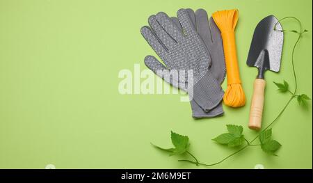 Utensili da giardino per la lavorazione di letti in giardino e guanti in tessuto su sfondo verde Foto Stock