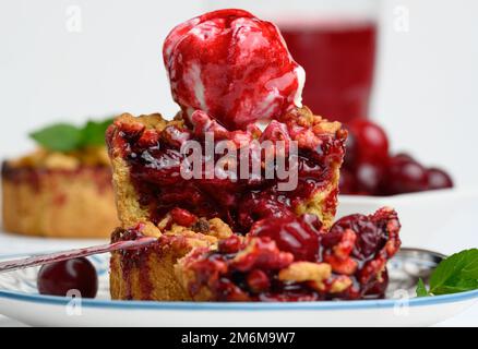 Torta crumble di ciliegie decorata con una paletta di gelato e condita con salsa di ciliegie Foto Stock