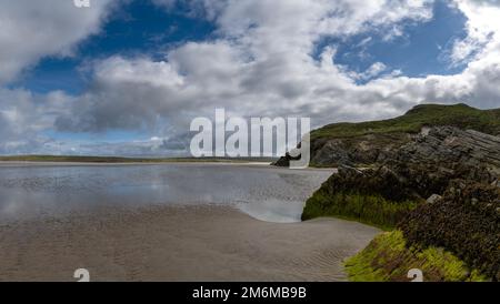 Vista sulla pittoresca spiaggia di sabbia dorata di Maghera, con rocce ricoperte di alghe e scogliere in primo piano Foto Stock