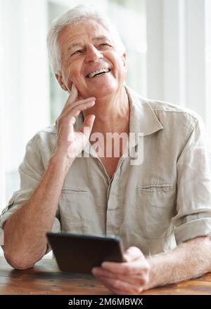 Il pensionamento mi ha dato così tanto tempo per esplorare nuove cose. Un uomo anziano felice che guarda lontano con attenzione mentre tiene un tablet digitale. Foto Stock