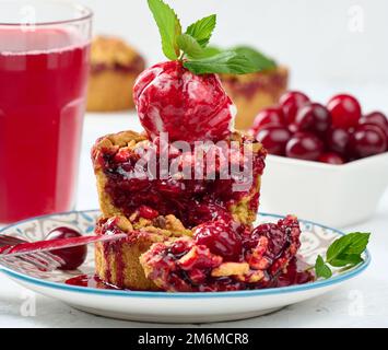 Torta crumble di ciliegie decorata con una paletta di gelato e condita con salsa di ciliegie Foto Stock