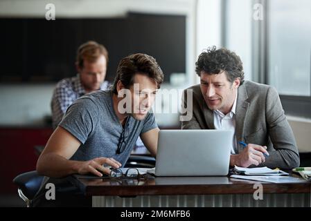 Ottenere una seconda opinione. due uomini d'affari che lavorano su un computer portatile in ufficio. Foto Stock