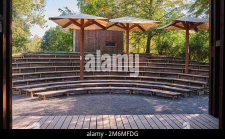 Posti a sedere vuoti spazio pubblico teatro all'aperto lunghe panchine in legno ombrello parco cittadino Foto Stock