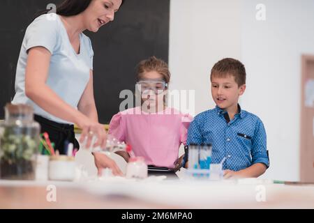 Scuola elementare Scienza Classe: Entusiasta insegnante spiega chimica a diversi gruppi di bambini, Little Boy Mixes Chem Foto Stock