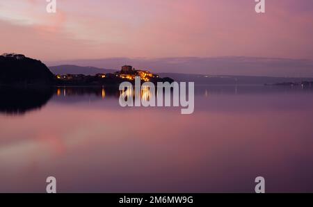 Lago di Bolsena e Capodimonte, una cittadina, in un roseo tramonto invernale. Panorama visto da Marta Foto Stock