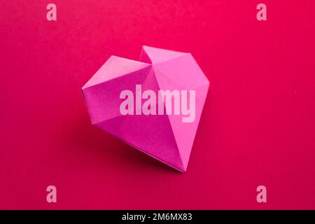 Origami di cuore di carta rosa isolato su uno sfondo rosso Foto Stock