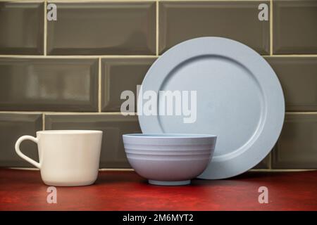 piatto piatto blu con tazza bianca di porcellana impilata in cucina su un piano di lavoro al linoleum rosso Foto Stock