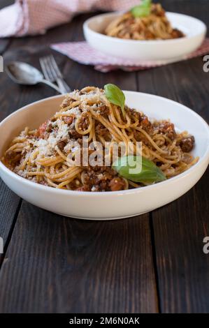 Spaghetti alla bolognese con parmigiano e foglia di basilico su un piatto su tavolo di legno con spazio per il testo. Cucina tradizionale italiana Foto Stock