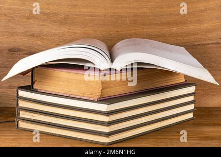 Vista in primo piano di una pila di libri oscuri con copertina rigida e un libro aperto di pagine bianche su un tavolo di legno. Foto Stock