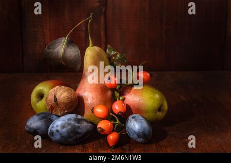 Pere e prugne con un ramo di rosa selvaggia su sfondo di legno scuro in stile rustico Foto Stock