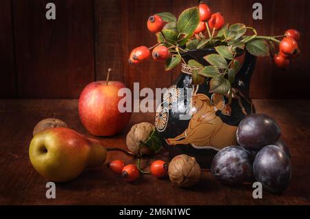 Pere e prugne con un ramo di rosa selvaggia su sfondo di legno scuro in stile rustico Foto Stock