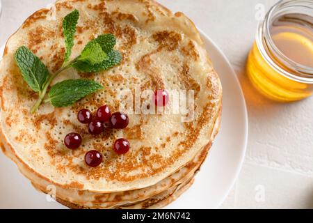 Pila di pancake fatti in casa serviti con miele e frutti di bosco, vista dall'alto Foto Stock