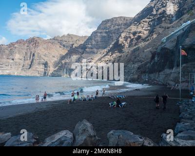 Los Gigantes, Tenerife, Isole Canarie, Spagna, dicembre 18, Giorno 2021: Spiaggia di sabbia nera vulcanica Playa de los Guios con gruppo di turisti che prendono il sole Foto Stock