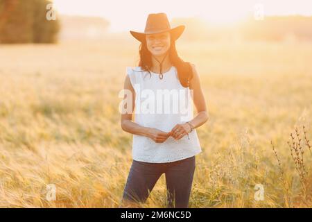 Donna contadina in cappello cowboy a campo agricolo al tramonto Foto Stock
