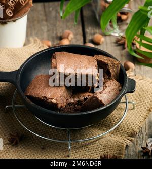 Pezzi di torta di brownie al cioccolato al forno con noci in una padella di metallo nero Foto Stock