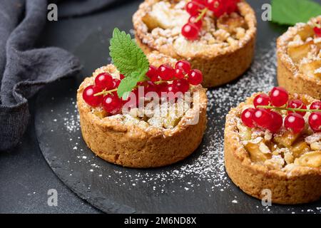 Crostata di frutta con ribes rosso cosparso di zucchero in polvere su un tavolo nero Foto Stock
