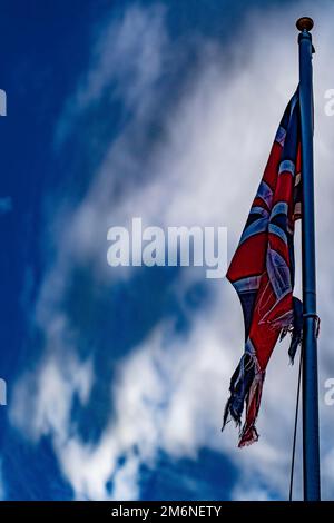 Bandiera di Union Jack lacerata e intaccata contro il cielo nuvoloso blu. Foto Stock