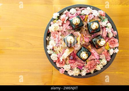 Vari dispenser di olio essenziale su vassoio circondato da petali di rosa per massaggi e spa, su superficie in legno Foto Stock