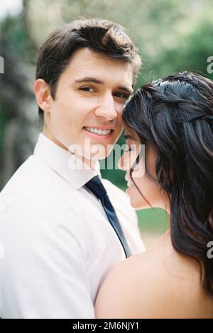 Sposa tocca la fronte alla guancia dello sposo sorridente. Verticale Foto Stock