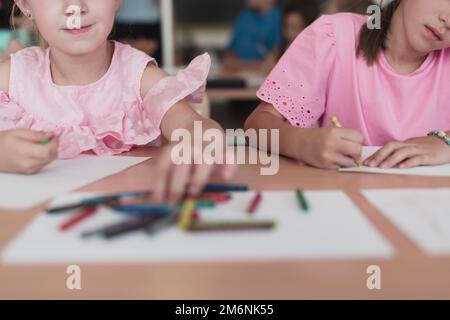 Bambine che si siedono nella scuola elementare disegnando su carta con i loro amici mentre si siedono in una classe moderna Foto Stock