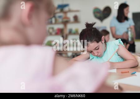 Bambine che si siedono nella scuola elementare disegnando su carta con i loro amici mentre si siedono in una classe moderna Foto Stock