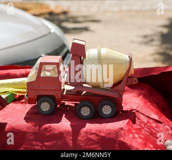 Su un tavolo c'è un'auto giocattolo rossa e gialla, un betoniere. Giocattoli per bambini. Foto Stock