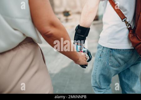 Giovane uomo disabile con mano protesica artificiale che cammina e tiene la mano della ragazza della donna. Foto Stock