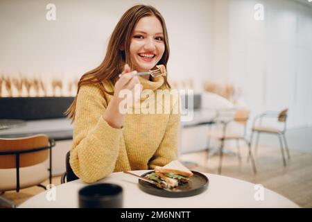 Giovane donna che mangia un panino al bar interno Foto Stock