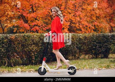 Giovane donna che guida scooter elettrico in autunno città Foto Stock