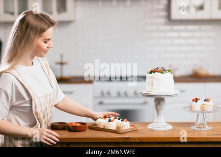 Pasticciere chef giovane donna caucasica con torta sul tavolo da cucina. Foto Stock