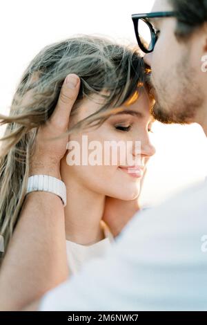 L'uomo bacia la donna sulla fronte, tenendo la testa tra le mani. Verticale Foto Stock