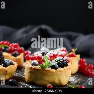 Crostata di frutta con ribes rosso cosparso di zucchero in polvere su un tavolo nero Foto Stock