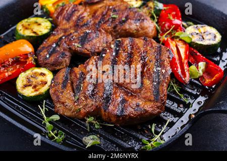 Tradizionale bistecca di maiale alla griglia con verdure grigliate servite e spezie in primo piano in una padella dal design rustico Foto Stock