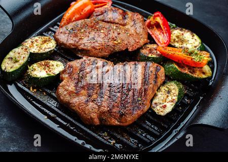 Tradizionale bistecca di maiale alla griglia con verdure alla griglia e spezie servite come primo piano in una padella dal design rustico Foto Stock