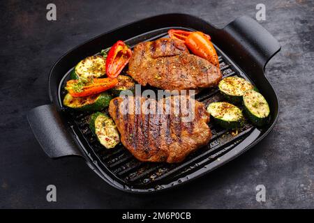 Tradizionale bistecca di maiale alla griglia con verdure alla griglia e spezie servite come primo piano in una padella dal design rustico Foto Stock