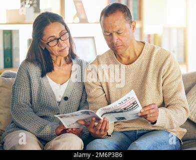 Coppia senior, lettura e giornale sul divano, concentrarsi o rilassarsi insieme al mattino per un evento globale. Uomo maturo, donna o carta media per internazionale Foto Stock
