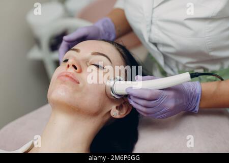 Primo piano della donna di testa che riceve la terapia facciale di phonoforesis di elettroporazione al salone di bellezza di centro termale. Foto Stock