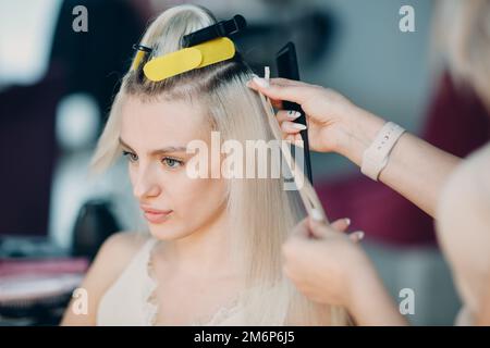 Parrucchiere femmina che fa estensioni di capelli a giovane donna con capelli biondi in salone di bellezza. Prolunga professionale per capelli. Foto Stock