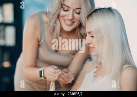 Parrucchiere femmina che fa estensioni di capelli a giovane donna con capelli biondi in salone di bellezza. Prolunga professionale per capelli. Foto Stock